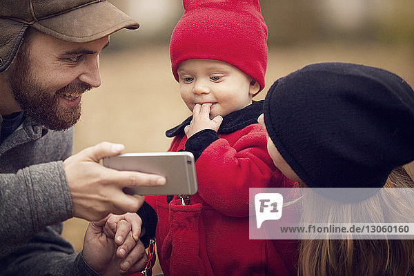 Vater zeigt dem Baby im Park ein Smartphone