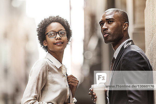 Businessman and businesswoman looking away while standing on city street
