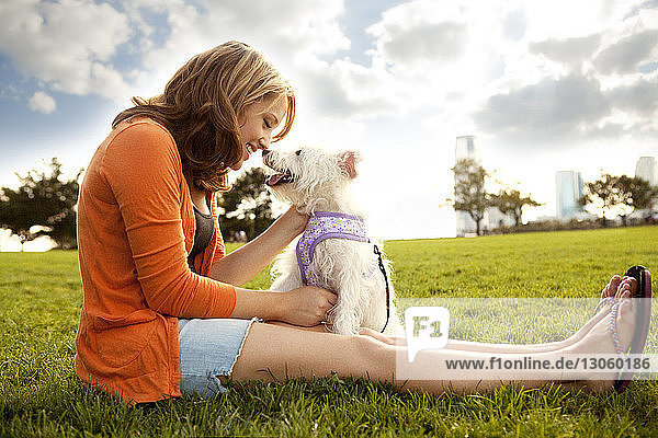 Glückliche Frau spielt an einem sonnigen Tag mit Hund auf Grasfeld