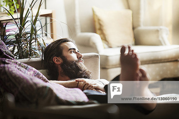 Man looking away while lying on sofa at home