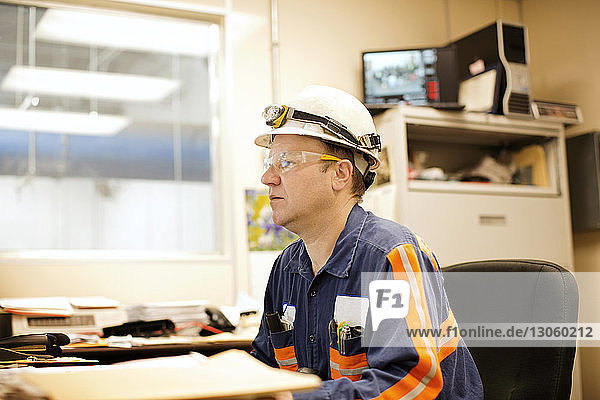 Side view of mature male worker sitting by table in recycling plant