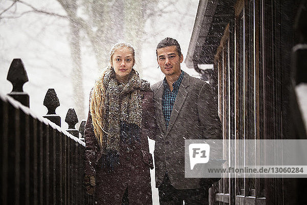 Portrait of couple standing by fence at forest during winter