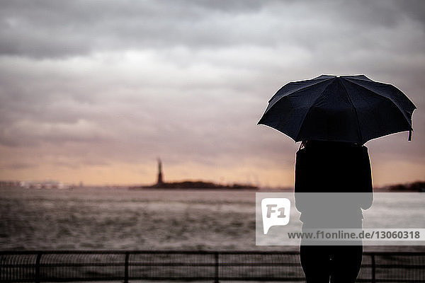 Rückansicht einer Frau mit Regenschirm vor bewölktem Himmel stehend