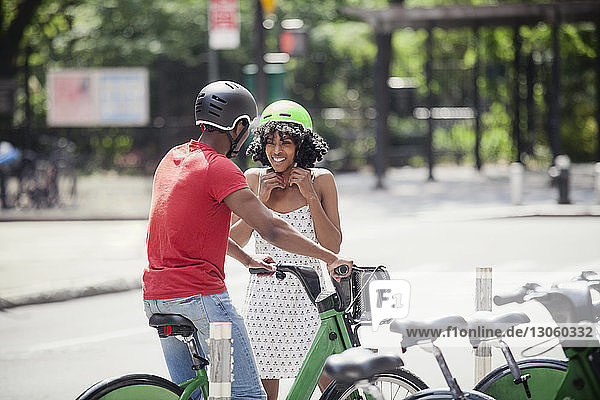 Man looking at woman fastening cycling helmet while standing on road
