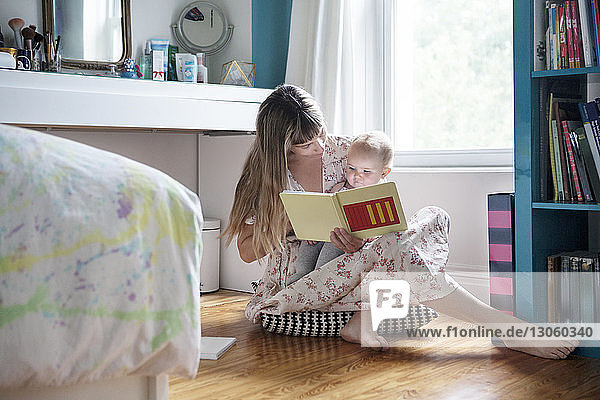 Mutter liest Buch mit Baby  während sie zu Hause auf dem Boden sitzt