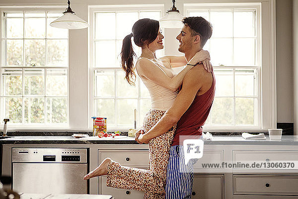 Happy couple embracing while standing in kitchen at home