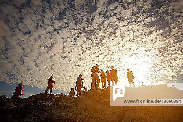 Low angle view of people on mountain against cloudy sky