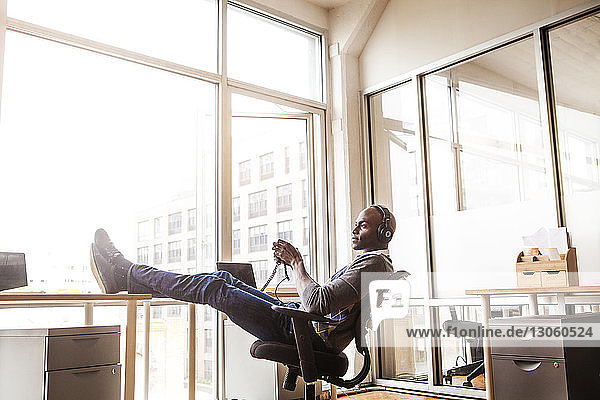 Seitenansicht eines Geschäftsmannes mit Kopfhörern,  der auf einem Stuhl im Büro sitzt