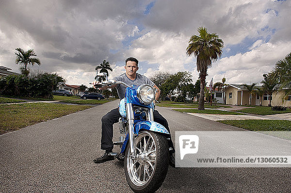 Man riding motorcycle on street against cloudy sky