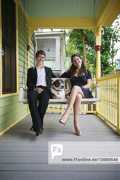 Porträt von glücklichen Freundinnen  die mit Hund auf der Schaukel auf der Veranda sitzen