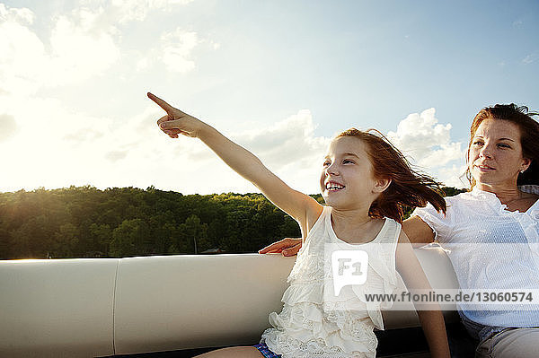 Glückliche Tochter zeigt beim Sitzen mit der Mutter im Boot gegen den Himmel