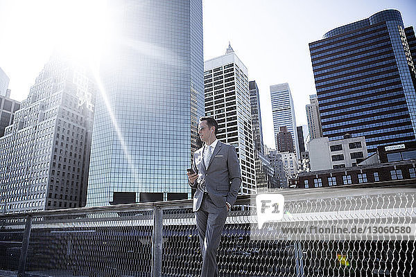 Geschäftsmann steht an sonnigen Tagen am Geländer vor Gebäuden in der Stadt