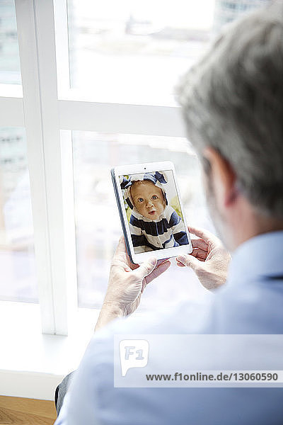 Rückansicht eines Mannes  der das Foto des Babys im Smartphone betrachtet