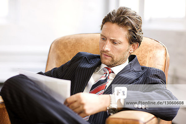 Geschäftsmann betrachtet Dokument  während er auf einem Sessel sitzt