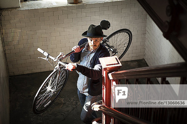 Hochwinkelansicht eines Mannes  der zu Hause ein Fahrrad auf einer Treppe trägt