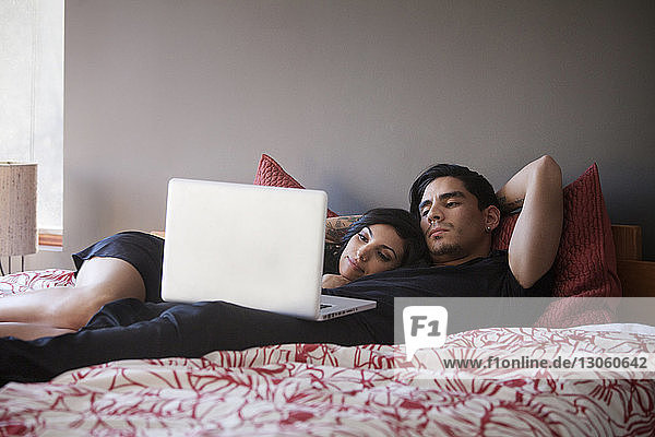 Couple looking at laptop computer while lying on bed at home
