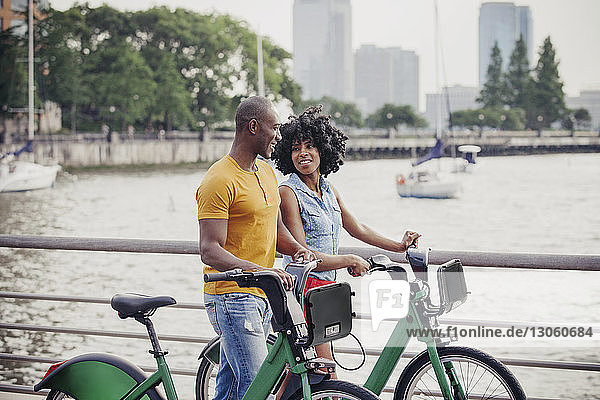 Couple with bicycles walking by railing against river