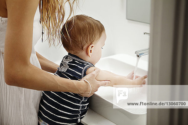 Ausgeschnittenes Bild einer Mutter  die dem Baby beim Händewaschen hilft