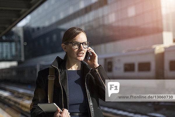 Businesswoman talking on phone while standing at railroad station platform