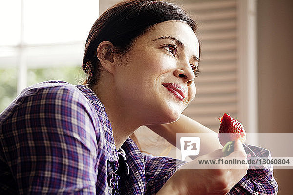 Glückliche Frau schaut weg  während sie eine Erdbeere hält