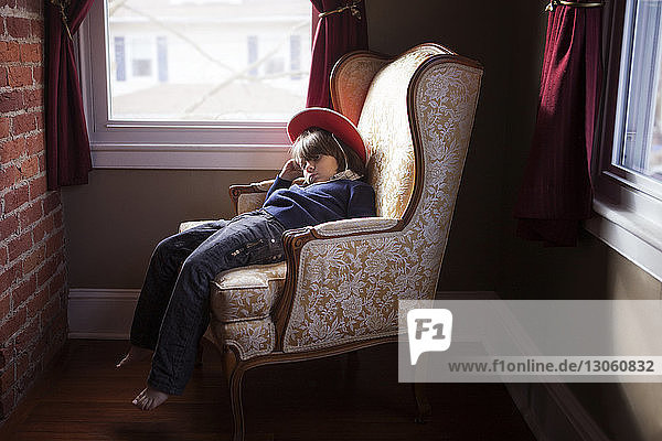 Boy wearing hat sitting on armchair at home