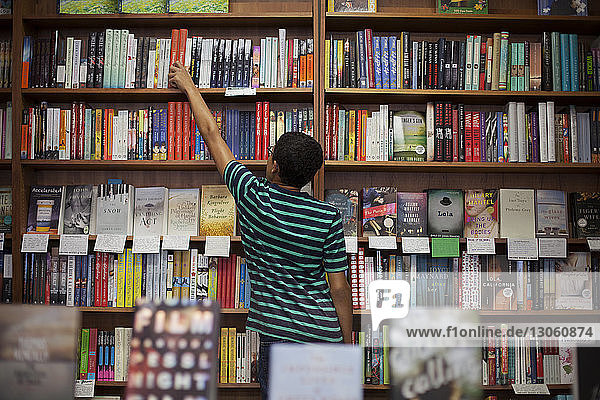 Rear view of man removing book from shelf while standing in store