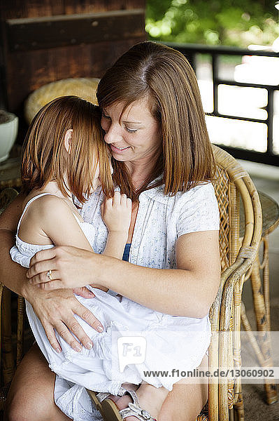 Mutter umarmt Tochter  während sie auf einem Stuhl sitzt