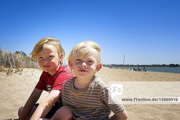 Porträt von Geschwistern  die am Strand auf Sand sitzen
