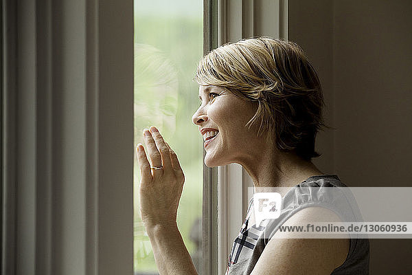 Fröhliche Frau schaut zu Hause durchs Fenster