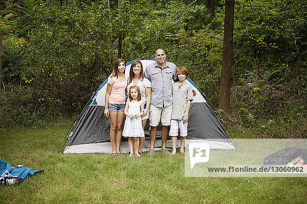 Porträt einer glücklichen Familie  die im Wald vor einem Zelt steht