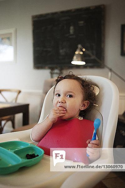 Kleines Mädchen isst  während es zu Hause im Hochstuhl sitzt