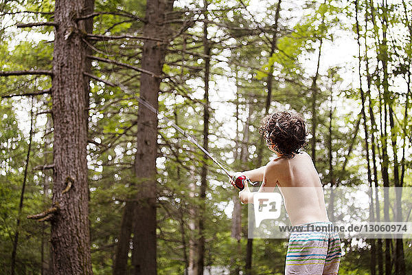 Rear view of boy casting fishing rod while fishing in forest