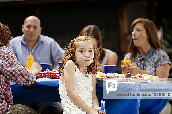 Portrait of girl sitting with family at picnic table