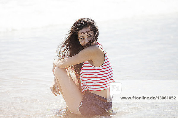 Seitenansicht einer nachdenklichen Frau  die am Strand am Ufer sitzt