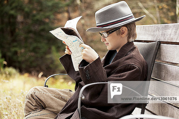 Junge liest Zeitung  während er auf einem Stuhl sitzt