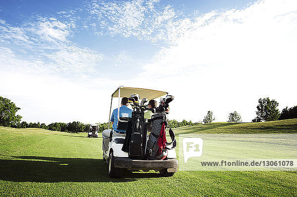 Rear view of friends riding in golf cart in field against sky