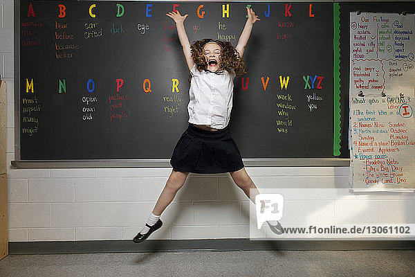 Excited schoolgirl jumping against blackboard in classroom