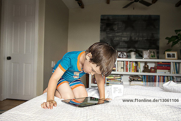 Boy looking at tablet computer while lying on bed at home