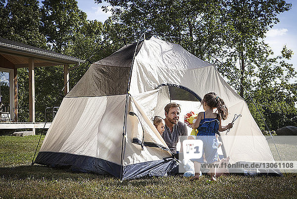 Father with children looking at girl while sitting in tent