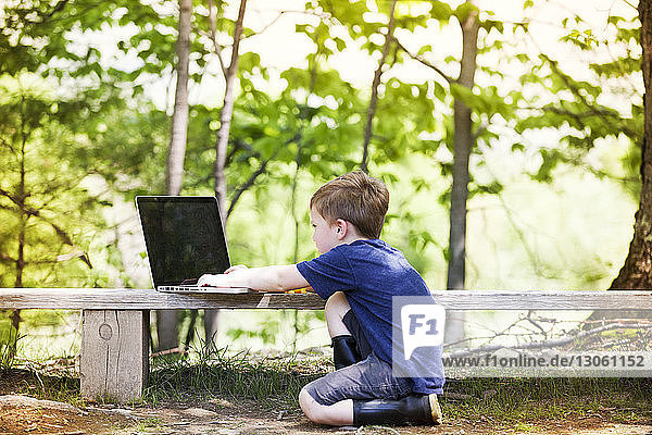 Seitenansicht eines Jungen mit Laptop-Computer auf einer Betonbank