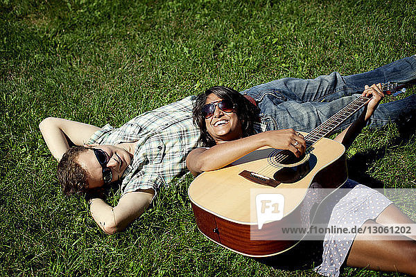 Hochwinkelaufnahme eines Paares mit Gitarre auf einem Grasfeld liegend