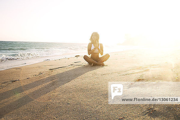 Frau meditiert  während sie am Strand auf Sand sitzt