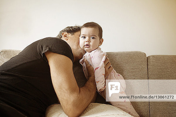 Seitenansicht eines Mannes  der seine Tochter küsst  während er zu Hause auf dem Sofa sitzt