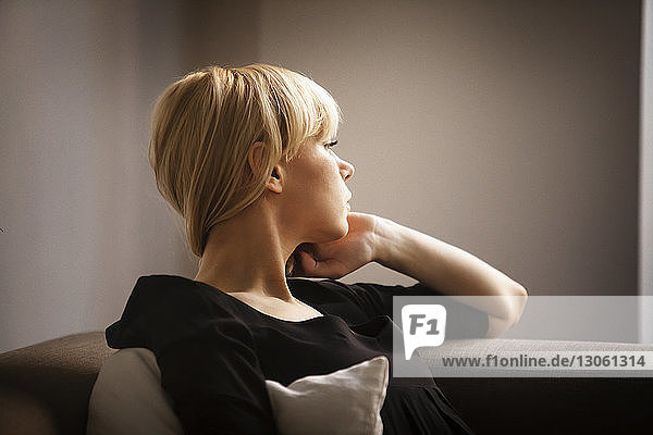 Young woman looking away while sitting on sofa at home