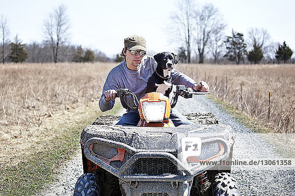 Man with dog riding quadbike on gravel road by field