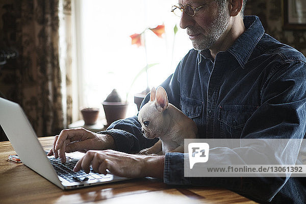 Mann sitzt mit Hund  während er zu Hause einen Laptop benutzt