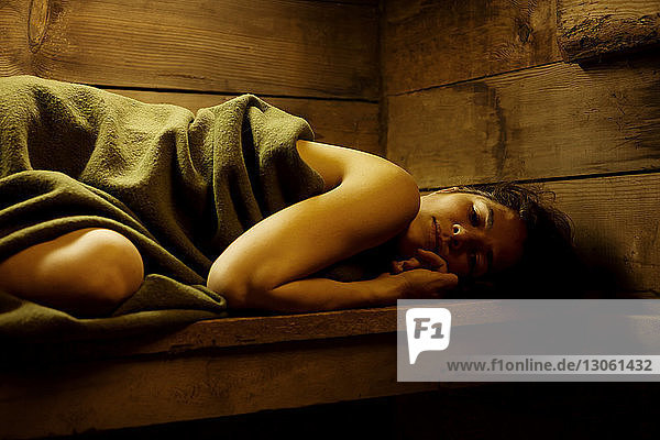 In eine Decke gewickelte Frau entspannt in der Sauna