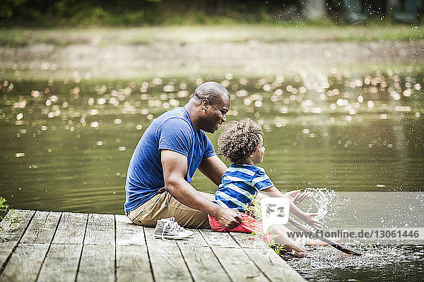 Glückliche Familie spritzt Wasser  während sie auf dem Steg am See sitzt