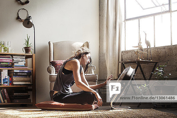 Seitenansicht einer Frau  die zu Hause vor einem elektrischen Ventilator sitzt