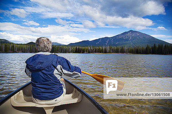 Rear view of man boating in lake towards mountain